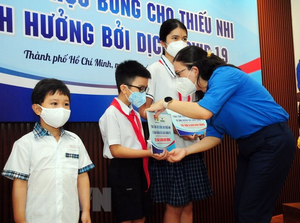Lãnh đạo Đoàn thanh niên Thành phố Hồ Chí Minh cùng các mạnh thường quân tặng học bổng cho các em học sinh mồ côi do dịch COVID-19. (Ảnh: Thanh Vũ/TTXVN)