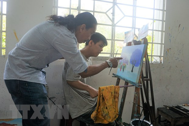 Thầy Nguyễn Văn Hoàng tỉ mỉ hướng dẫn học sinh của mình cách chọn phối màu. (Ảnh: Thu Hoài/TTXVN)